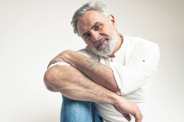 Beyaz gömlek ve kot pantolon giyen gri saçlı adam beyaz arka planda izole edilmiş kamera için poz veriyor. Yüksek kalite fotoğraf