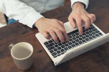 Dizüstü bilgisayarı üzerinde çalışan bir adamın elleri boş bir fincan kahveyle birlikte ahşap bir masaya yerleştirilmiş. Yüksek kalite fotoğraf