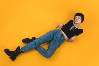 Model konsepti. Turuncu arka plan. Yüksek açılı atış. Kısa saçlı kadın tek bacağı bükülmüş ve kameraya bakıyor. Yüksek kalite fotoğraf