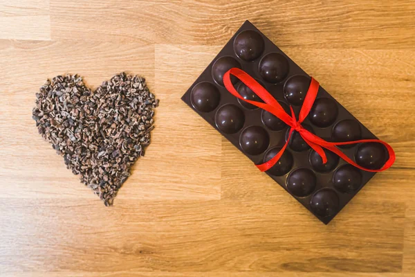 Sweet love. Love for sweets concept. Origin of chocolate. Dark bar of chocolate with red ribbon lying next to a heart made of grounded cocoa seeds. Copy space. . High quality photo