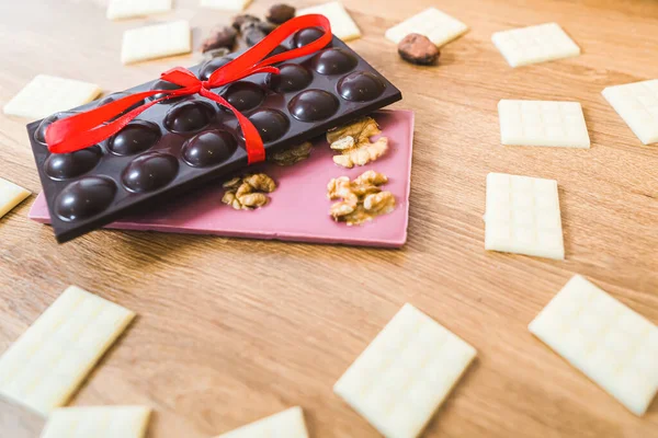 Sweet gift concept. Chocolate bars of various flavours on wooden table. Dark chocolate, ruby chocolate, and white chocolate as decoration. High quality photo