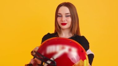 Amerikan futbol kaskı tutan hoş görünümlü bir amigo kız, orta boy yakın plan, sarı arka plan. Yüksek kalite 4k görüntü