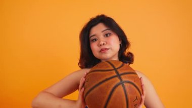 Siyah saçlı kısa saçlı ponpon kız elinde bir basket topuyla kameraya doğru, yakın plan, turuncu arka plan. Yüksek kalite 4k görüntü