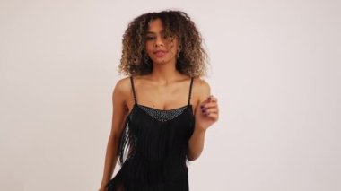 Siyah elbiseli, kıvırcık saçlı dansçı beyaz arka planda dans ediyor, orta boy. Yüksek kalite 4k görüntü