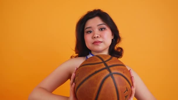 Młoda Cheerleaderka Pokazuje Koszykówkę Kamery Odizolowanej Pomarańczowym Tle Wysokiej Jakości — Wideo stockowe