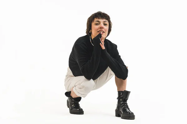 stock image Crouching smiling short haired woman in black sweater, boots and bright trousers on white background