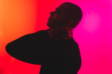 Stresli bir adam iki parmağıyla boynunun arkasına dokunuyor. Neon pembe arka planda koyu renk erkek silueti. Yüksek kalite fotoğraf