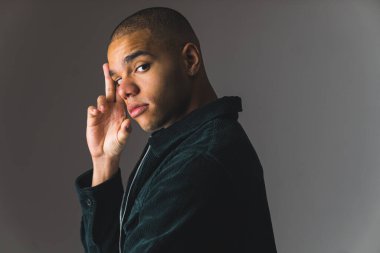 Kendine güvenen ciddi bir adam alnına dokunuyor ve kameraya bakıyor. Gri arka planda poz veren erkek model. Yüksek kalite fotoğraf