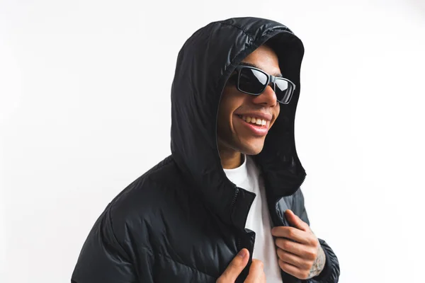 ブラックのパッパージャケットとサングラスのハンサムなブラックの男性モデルはフード付きで笑顔 屋内の肖像画を閉じます 白地だ コピースペース 高品質の写真 — ストック写真