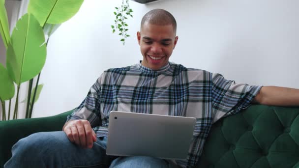 若い男性起業家は銀製のラップトップで緑のソファに座っています ビジネスコンセプトの進化 アパートのインテリア 高品質4K映像 — ストック動画