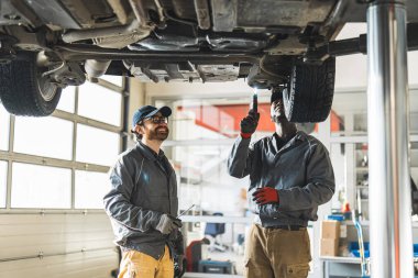 Garajda arabanın altında çalışan çok ırklı mekanikçilerin orta ölçekli görüntüleri. Yüksek kalite fotoğraf