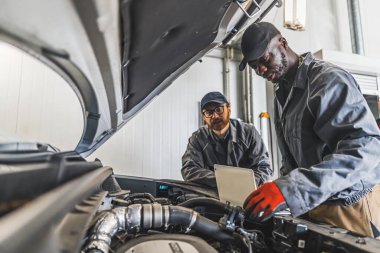 Araba motoru kompartımanının yanında dizüstü bilgisayar kullanan iki tamircinin orta ölçekli görüntüsü. Yüksek kalite fotoğraf