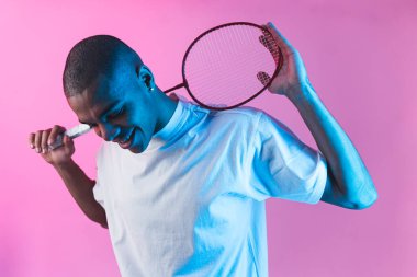 Stüdyo arka planında tenis raketi olan, neon ışıklı, gülümseyen Afrikalı genç bir adam. Yüksek kalite fotoğraf