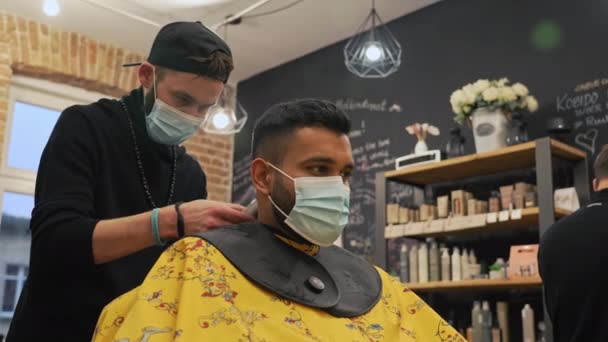 理发师在理发店里用修剪过的发型师把男顾客的头发修剪得整齐一些 两人在大流行时都戴着口罩 高质量的4K镜头 — 图库视频影像