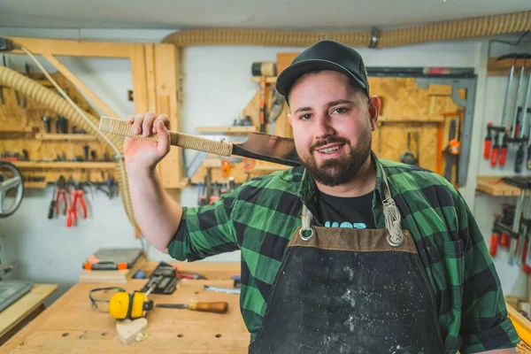 Stock image Woodworking tools concept. Positive male adult carpenter holding one of his tools and looking at camera with a smile. Workshop interior. High quality photo