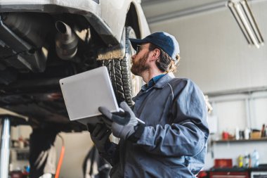 Bir araba tamircisi dizüstü bilgisayar tutuyor ve garajdaki arabaya bakıyor, orta ölçekli. Yüksek kalite fotoğraf