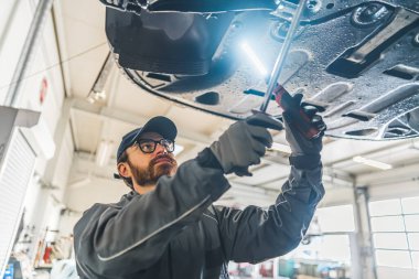 Bir otomobil tamircisinin şasi denetimi ve araba atölyesi için özel aletler kullanarak araba üzerinde çalışırken orta ölçekli yakın çekimi. Yüksek kalite fotoğraf