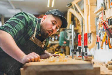 Ahşap işçiliği sırasında ahşap dolgulara üfleyerek yeni ahşap ürünler üreten odaklanmış erkek marangoz. - Evet. Yüksek kalite fotoğraf