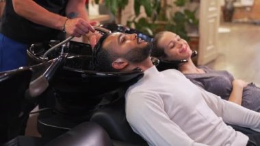 Kafasını şampuan kasesinde yıkarken kuaförde hamile karısı olan neşeli Hintli bir adam saçını yıkıyor. Yüksek kalite 4K görüntü