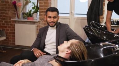 Hintli bir adam, bir güzellik salonunda saçını yıkatan karısıyla konuşuyor. Yüksek kalite 4k görüntü