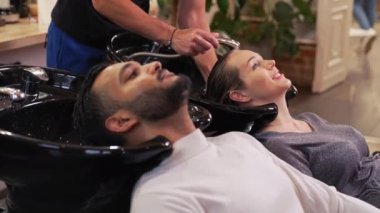 Kuaför salonundaki genç bir çift saçını yıkarken kafasını şampuan kasesine yaslıyor. Yüksek kalite 4k görüntü