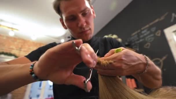 若い女性の長いブロンドの髪を切断サロンで美容師トリミング髪に焦点を当て 高品質4K映像 — ストック動画