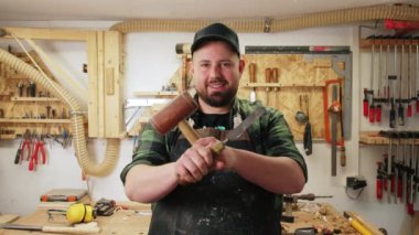 Genç bir marangozun aletlerini tuttuğu ve atölyesinde gülümsediği orta boy bir fotoğraf. El işi konsepti. Yüksek kalite 4k görüntü