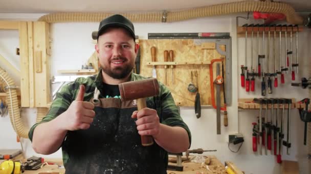 一个笑着拿着锤子的木匠在一个木工工作室里竖起大拇指 高质量的4K镜头 — 图库视频影像