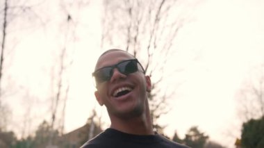 Güneş gözlüklü, güneşli ve temiz havanın tadını çıkaran neşeli, yakışıklı bir adam. Açık havada yakın çekim. Yüksek kalite 4k görüntü