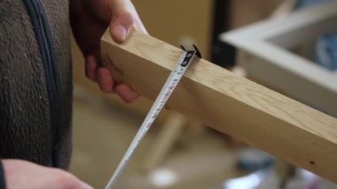 Erkek marangoz, metal bir mezura kullanarak ahşap bir tahtanın ölçümlerini alıyor. Yüksek kalite 4k görüntü