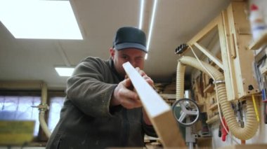 Marangoz ahşap bir tahta parçasını ahşap bir makine kullanarak düzleştirdikten sonra inceliyor. Yüksek kalite 4k görüntü