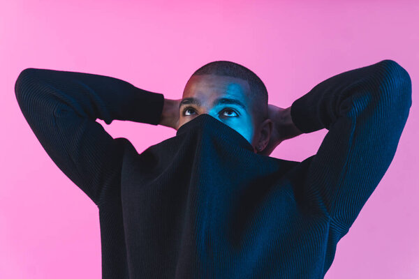 Bald man covering half face with his black sweater and looking up, pink background medium closeup. High quality photo