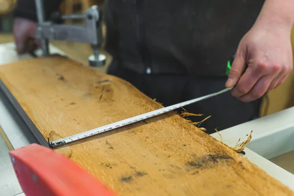 Stock image closeup shot of carpenter measuring a wooden piece with a tape measure, working on wood. High quality photo