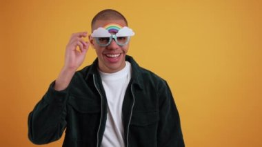 Sarı arka planda gökkuşağı şeklinde güneş gözlüğü takan genç ve neşeli bir Afro-Amerikalının yakın çekimi. Yüksek kalite fotoğraf