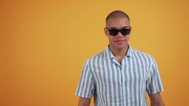 Afroamerykański Przystojniak Okularach Przeciwsłonecznych Koszulce Paski Wycelowanej Obok Pomarańczowym Tle — Wideo stockowe