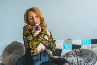 Kızıl saçlı beyaz kadın, kanepede otururken sevgili Devon Rex kedisine sarılıyor. Yüksek kalite fotoğraf