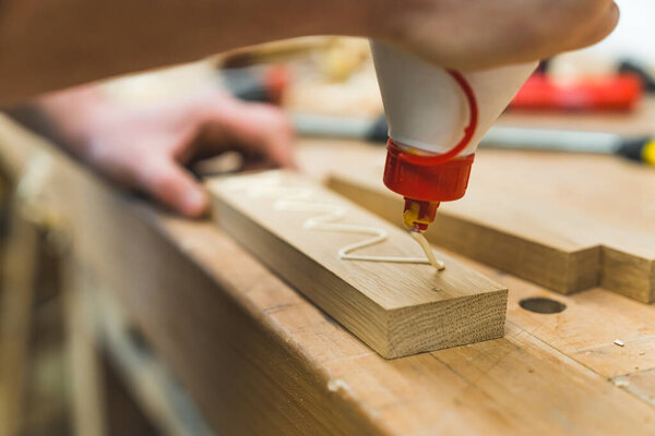 Carpenter spreads glue on wooden pieces using a brush in a woodworking studio. High quality photo