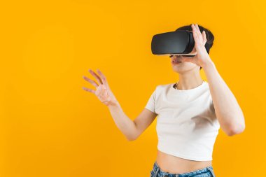 Beyaz bluzlu bir kadın VR kulaklıkla oynuyor. Boş zaman konsepti. Parlak sarı arka plan. Yüksek kalite fotoğraf