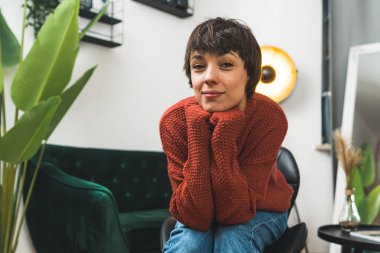 Genç bir kadın, gizemli bir ifadeyle kameraya bakıyor ve dirseklerini dizlerinin üzerine eğiyor. Yüksek kalite fotoğraf