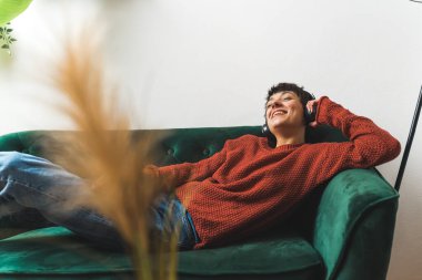 Boş zaman konsepti. Ön planda bulanıklık. Yeşil bir kanepede uzanmış müzik dinlerken gülümseyen bir kadın. Yüksek kalite fotoğraf