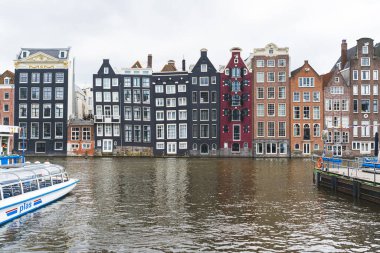 Amsterdam 'daki Dansçı Evleri. Kanal boyunca renkli yüksek binalar inşa edildi. Damrak Kanalı 'nda dans eden evler. Hava bulutlu. Yüksek kalite fotoğraf