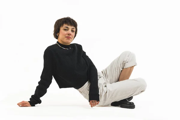 一个身穿黑色套头衫和白色长裤的女人 双腿交叉坐在一起 一只手靠在地上的全景照片 高质量的照片 — 图库照片
