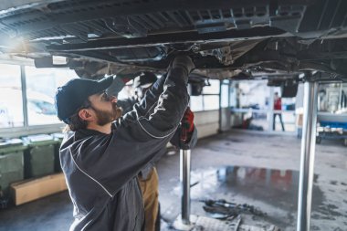Otomobil tamircisi adamlar servis dükkanında asansörle kaldırılmış araba şasisi tamir ediyorlar. Yüksek kalite fotoğraf