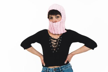 Beyaz arka planda poz veren genç bir kadın kot pantolon, siyah bir bluz ve pembe bir kar maskesi giyiyor. Yüksek kalite fotoğraf