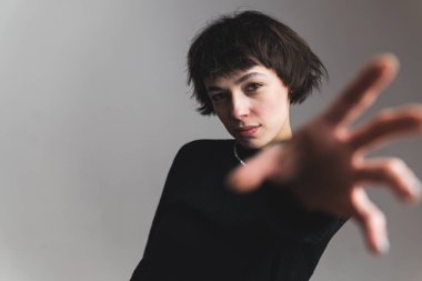 Elini öne uzatıp kameraya bakan güzel bir kadın modelin orta boy görüntüsü. Gri arka plan. Yüksek kalite fotoğraf