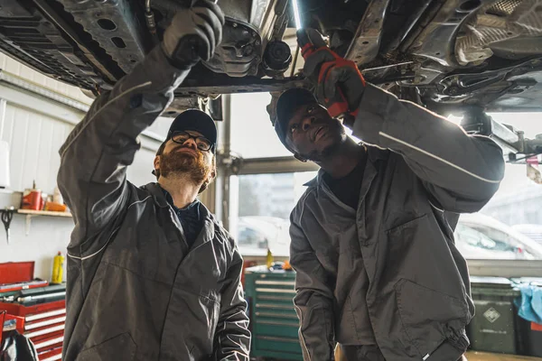 Två Bilservicearbeten Reparerar Fordonschassit Stående Det Högkvalitativt Foto — Stockfoto
