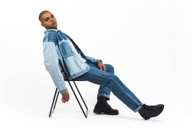 Siyah kot elbiseli bir manken beyaz bir arka plana karşı siyah bir sandalyede poz veriyor. Yüksek kalite 4k görüntü