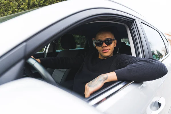 Black handsome young man with tattooed hand sits in the driving seat of the car. High quality photo
