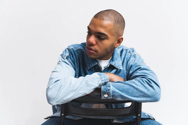 Stock image Young African American guy in denim shirt sitting on reversed chair looking away. High quality photo