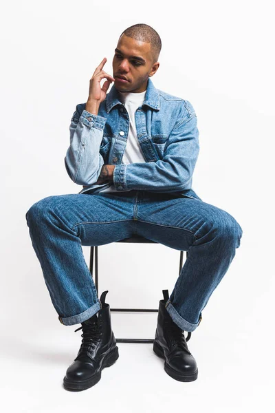 stock image Black model in denim clothes posing on a black folding chair against a white background. High-quality 4k footage
